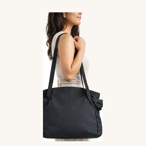 The black convertible tote carried on the shoulder, gathered closed by its drawstrings